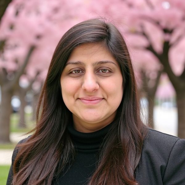 A woman smiling outdoors with pink blossom trees in the background.
