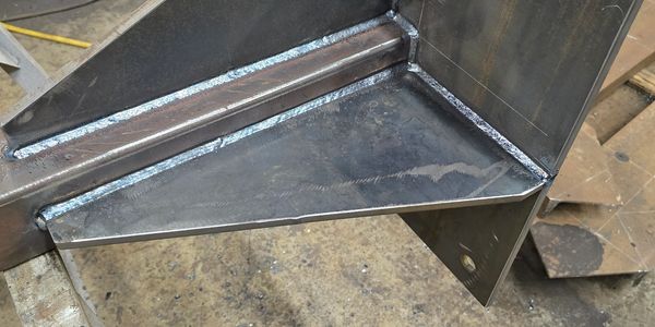 Close-up of a welded metal bracket with clean welds in a workshop.