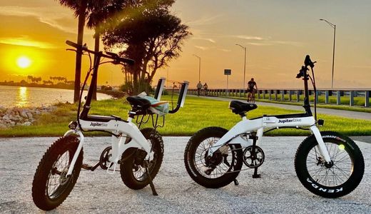 2 electric bikes in foreground, beach and sunset in background. www.whatsuppaddlesports.com