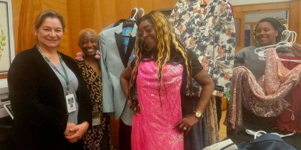 Four people smiling with clothing racks in a room.