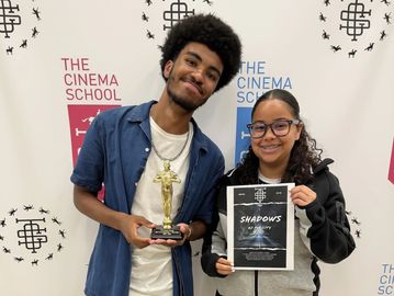 Two people smiling with an award and certificate at The Cinema School.