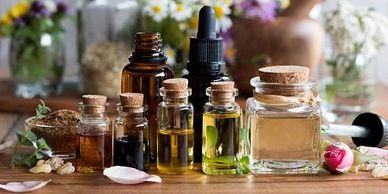 Various essential oil bottles with cork stoppers on a wooden surface surrounded by flowers.