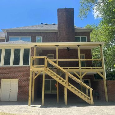 Newly constructed wooden deck with stairs attached to a brick house.