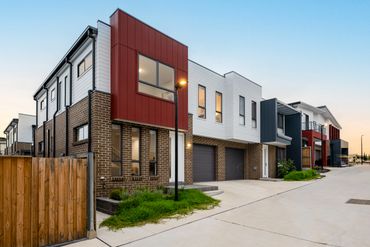 Modern townhouses with brick and panel exteriors on a clean street at dusk.