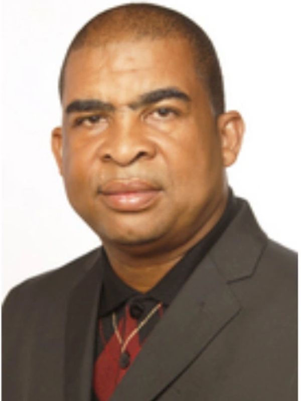 Portrait of a man in a dark suit with a red and black shirt.