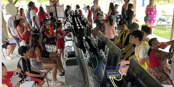 People gathered under a pavilion engaging with computers and gaming consoles.