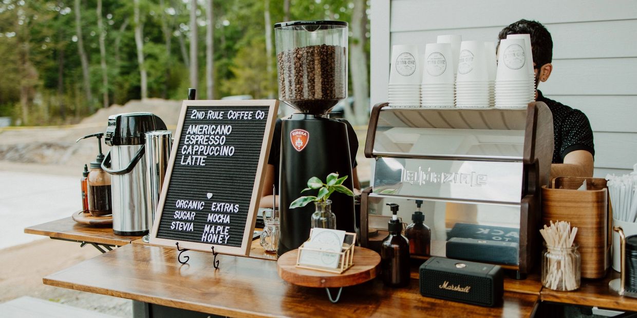Outdoor coffee stand with espresso machine, grinder, and menu board.