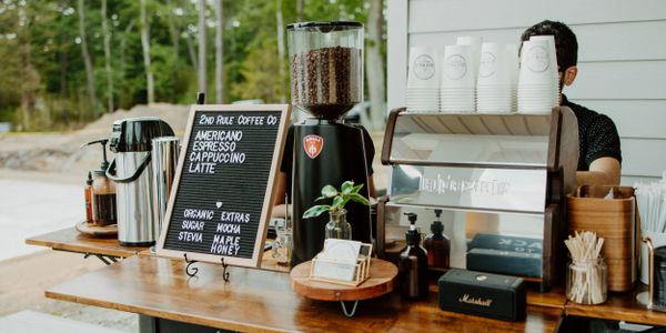 Outdoor coffee stand with espresso machine, grinder, and menu board.