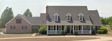 Country farmhouse style with covered porches and dormers at second floor bedrooms.