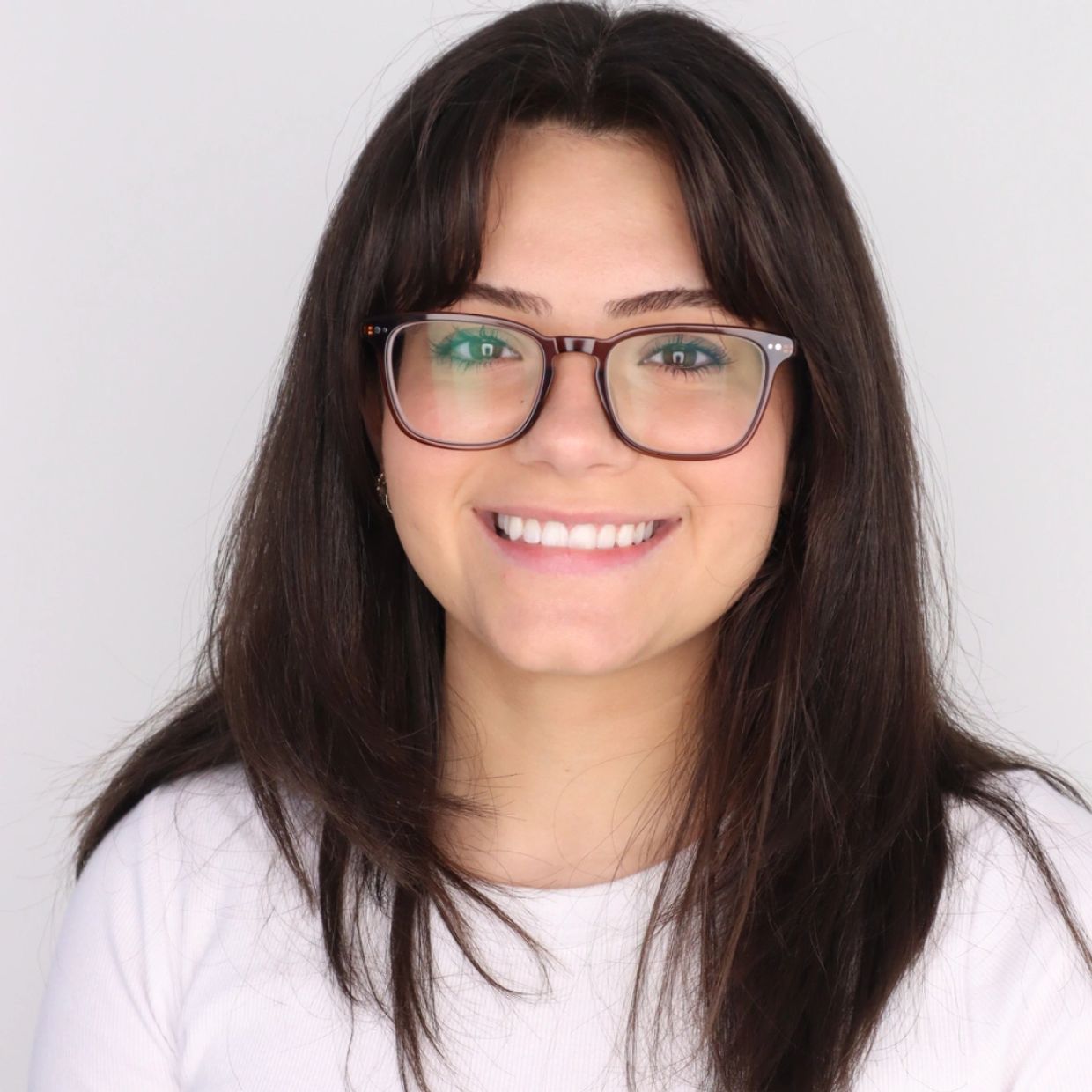 Young woman with glasses smiling against a plain background.