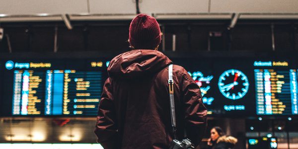 Person in red jacket looking at flight departure board at airport.
