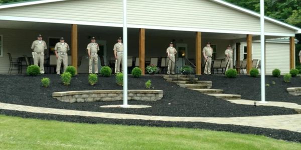 Seven uniformed individuals standing on a porch of a building with landscaped garden in front.
