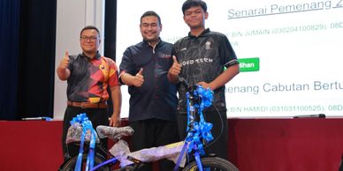 Three men giving thumbs up beside a bicycle decorated with blue ribbons.