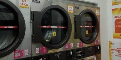 Three industrial laundry machines with open doors in a laundromat.
