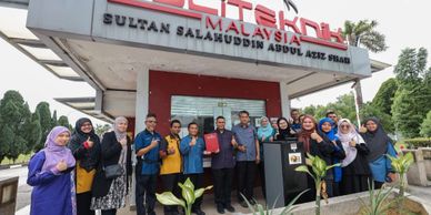 Group of people posing outside a Malaysian building with thumbs up.