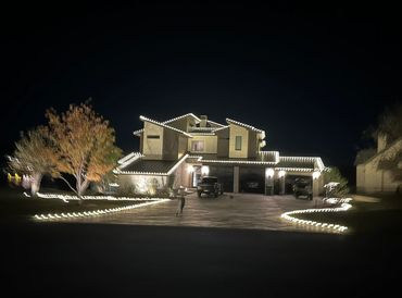 A house decorated with string lights along the roof and driveway at night.