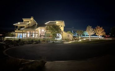Modern house decorated with white string lights and a Christmas tree inside at night.