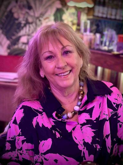 Smiling woman wearing a vibrant pink and black floral blouse and beaded necklace.