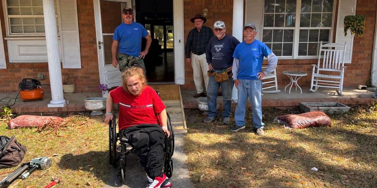 A young man in a wheelchair with four men standing outside a brick house.