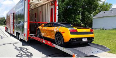 A yellow sports car being loaded into a large red and silver enclosed trailer.