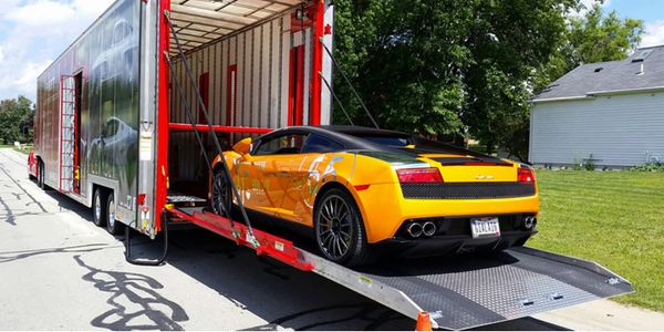 Yellow sports car being loaded into a trailer on a sunny day.