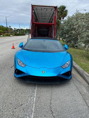 A blue Lamborghini parked in front of an open car transport trailer on a street.