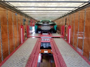Sports car loaded above an autonomous delivery vehicle inside a transport trailer.