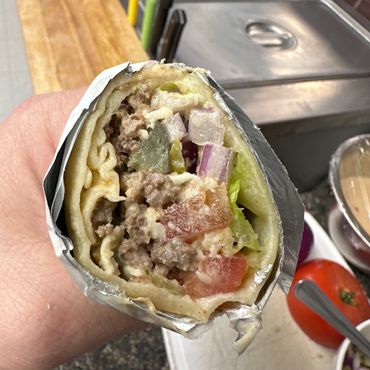 Close-up of a wrapped gyro with meat, tomatoes, onions, and lettuce.