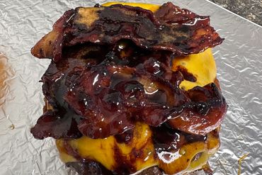 Cheeseburger topped with crispy bacon and a glossy sauce on foil.