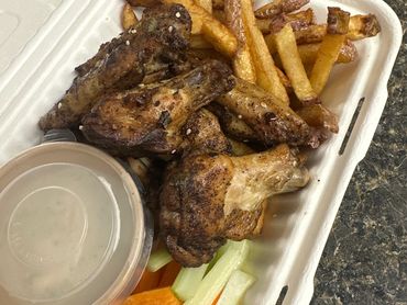 Takeout container with chicken wings, fries, carrots, celery, and dipping sauce.