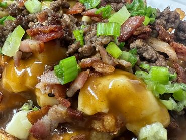 Loaded poutine with gravy, cheese curds, ground beef, bacon, and green onions.