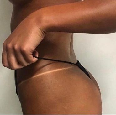 Close-up of a person adjusting black bikini bottoms showing a tan line.