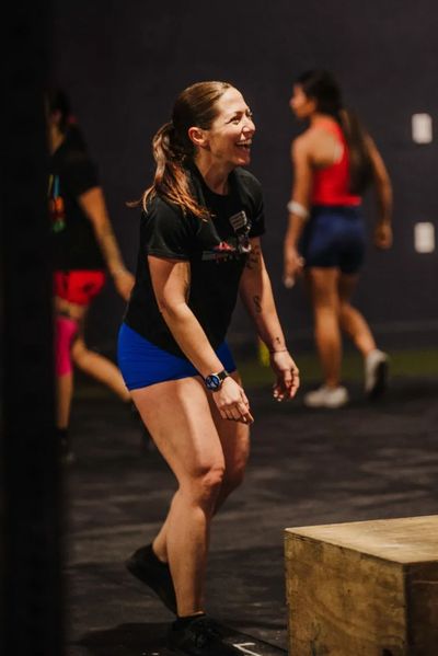 Woman smiling and exercising by a wooden box in a gym.