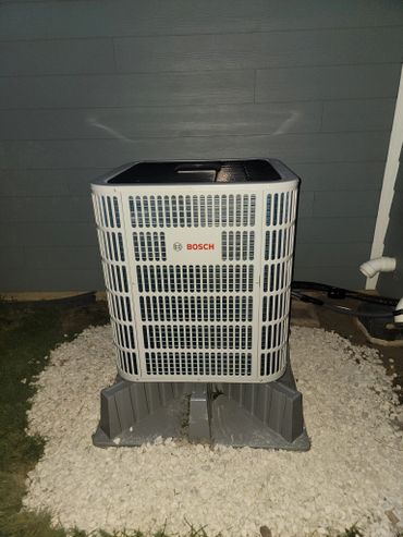 Bosch air conditioning unit installed outside a house at night.