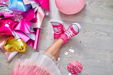 Child's legs in pink sneakers surrounded by party decorations and balloons.