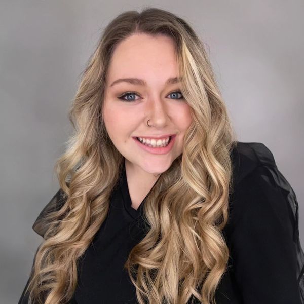 Smiling woman with long blonde curly hair and nose ring.