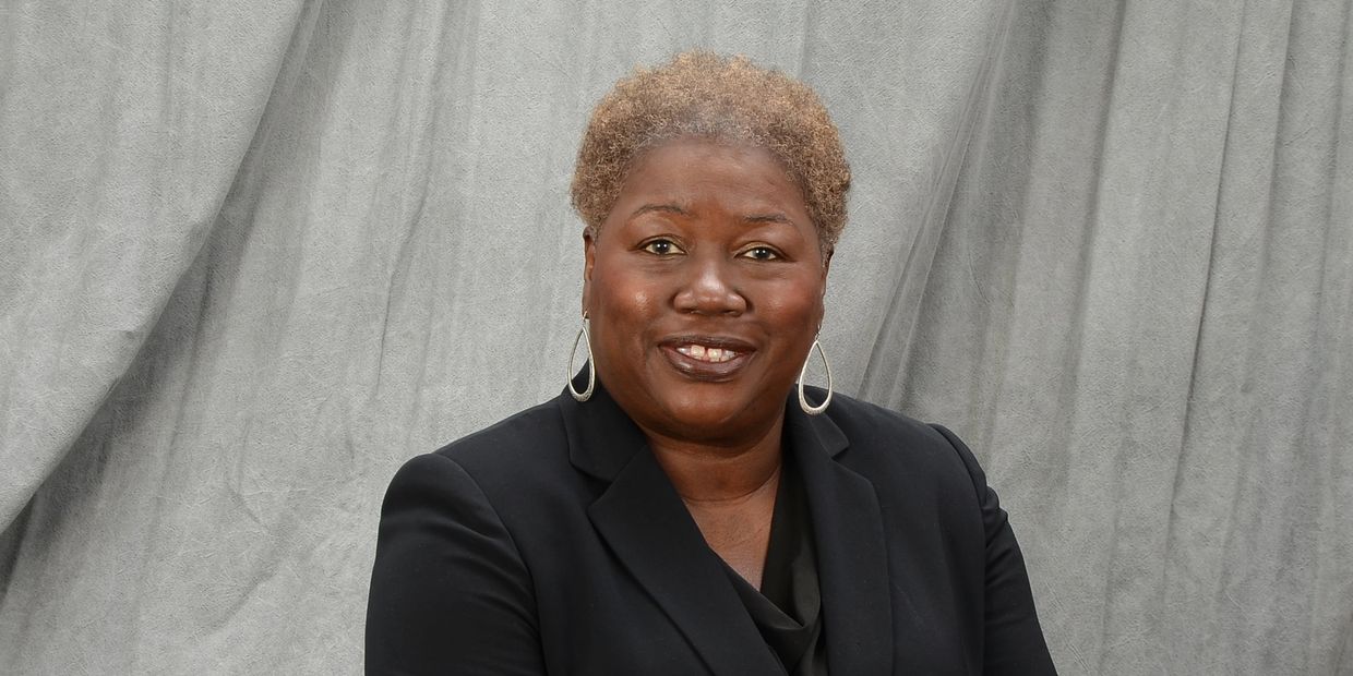 Confident woman in black blazer posing against a gray backdrop.