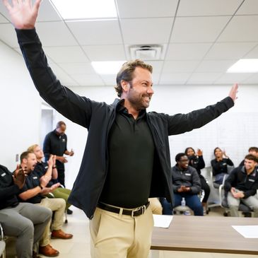 Man joyfully raises arms while colleagues applaud in a meeting room.