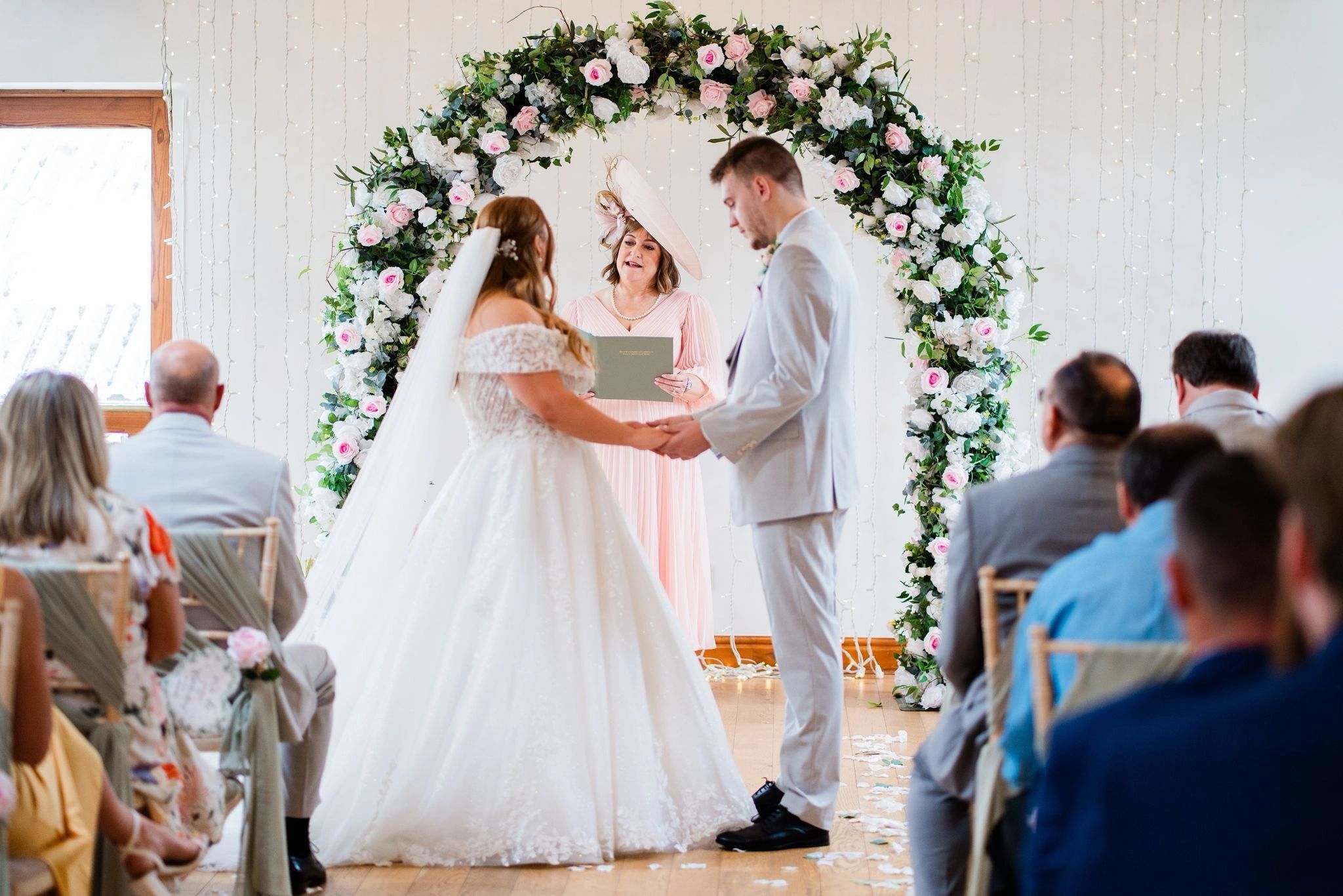 Bride and groom holding hands during wedding ceremony under floral arch.