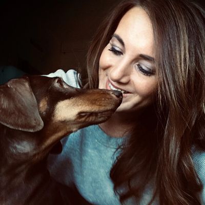 A woman smiling as her dog nuzzles her nose affectionately.