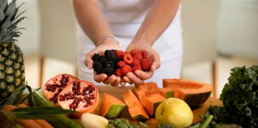 Hands holding fresh raspberries and blackberries over various fruits.