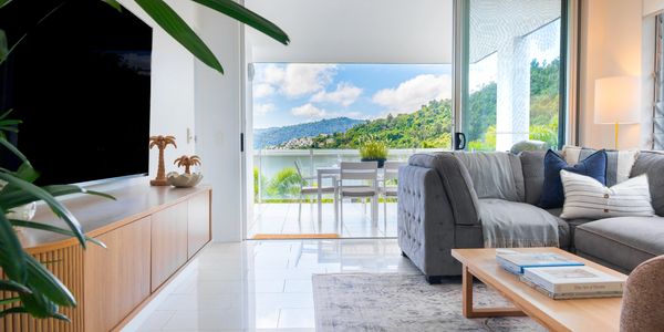 Bright living room with gray sofa and mountain view through sliding glass doors. Airlie Beach Apartment, Vacation Rental, Whitsundays Accommodation.