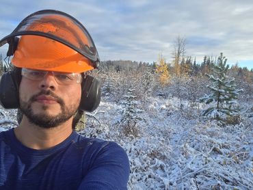 Man in safety gear takes a selfie in a snowy forest.