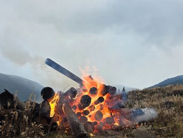 A pile of logs burning intensely in an open field.