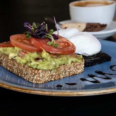 Avocado toast topped with tomato slices and microgreens, served with poached eggs and coffee.