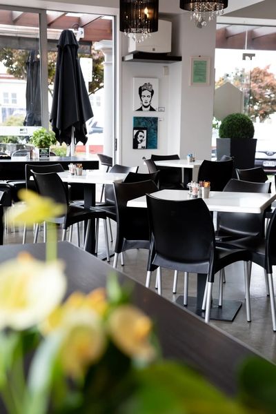 Modern cafe interior with black chairs and white tables, decorated with art and plants.
