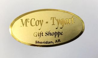 A photo of a golden sticker. It is oval-shaped and reads "McCoy-Tygart Gift Shoppe Sheridan, AR."