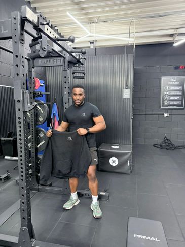 Man holding a sweatshirt in a gym, standing next to workout equipment.