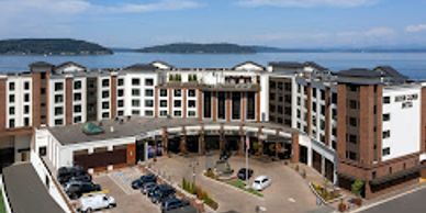 Large hotel building near water with parked cars.