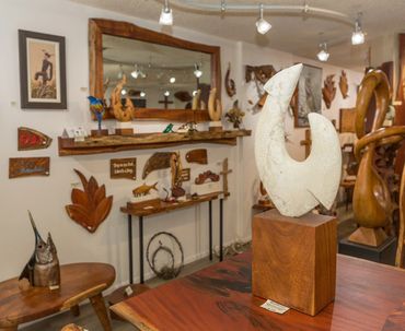 Interior of the gallery featuring wood sculptures, wall art, and a large white fish hook sculpture.